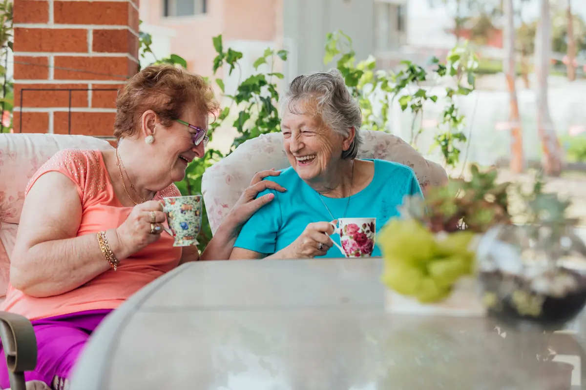 Two older women laughing over a cup of tea
