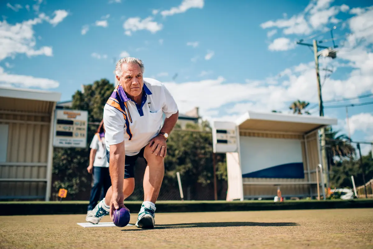 An older man bowling on a lawn bowls green